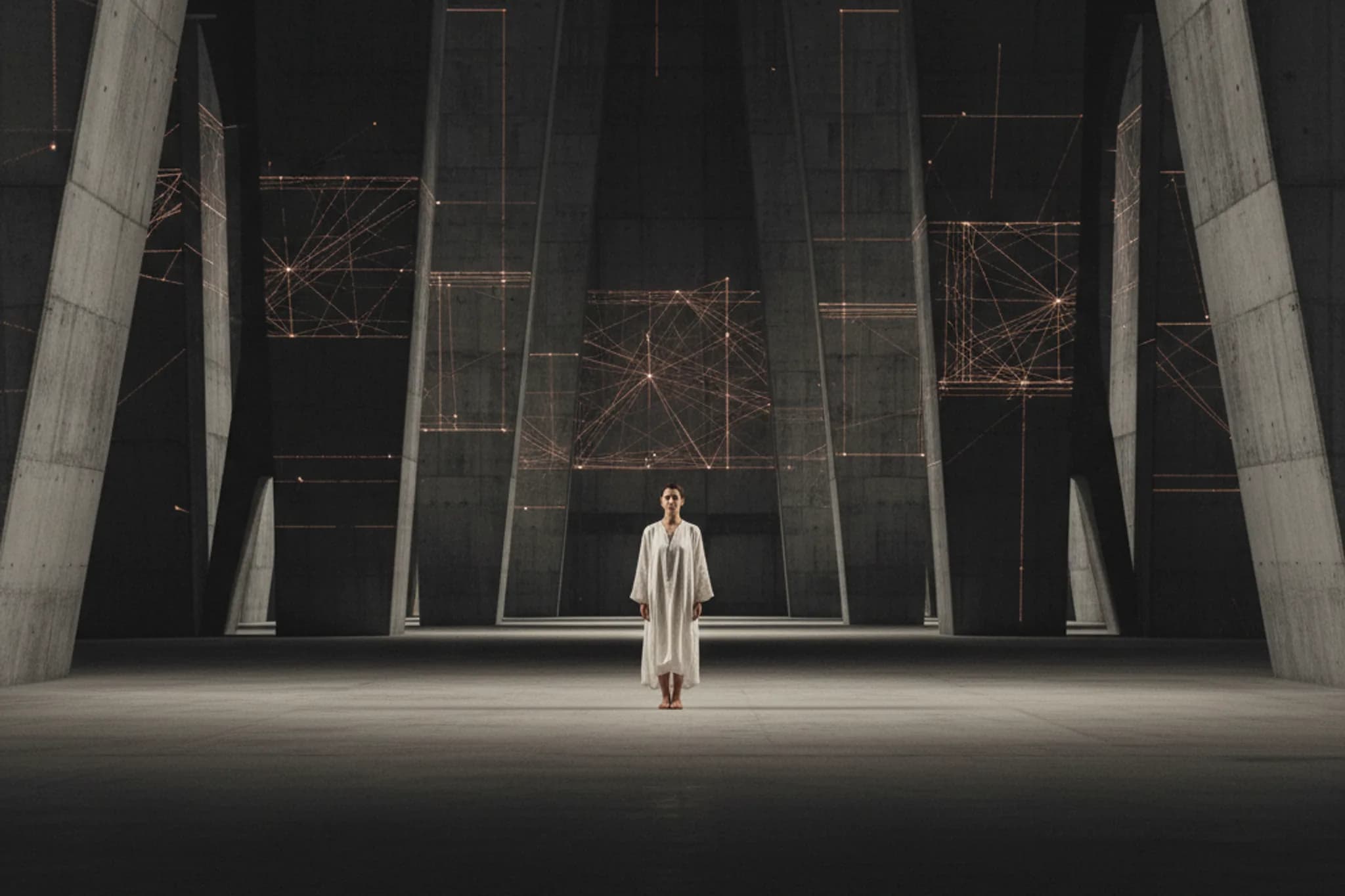 Solitary human figure standing calmly in a vast dark architectural space, with faint geometric networks of light suggesting machine intelligence at infrastructure scale